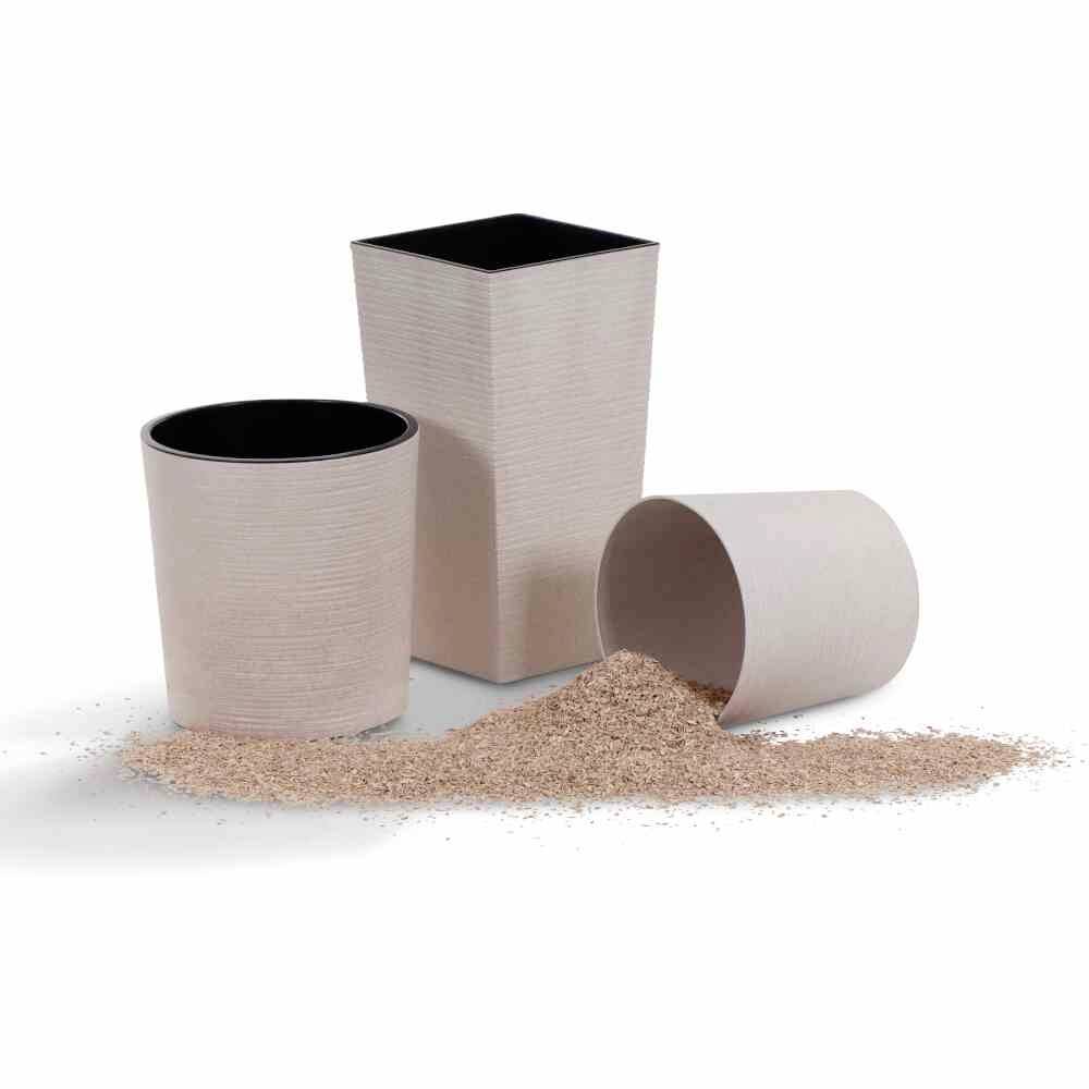 Drei umweltfreundliche Blumentöpfe aus recyceltem Material, einer liegt umgekippt mit verstreuten Holzspänen, die anderen stehen aufrecht.