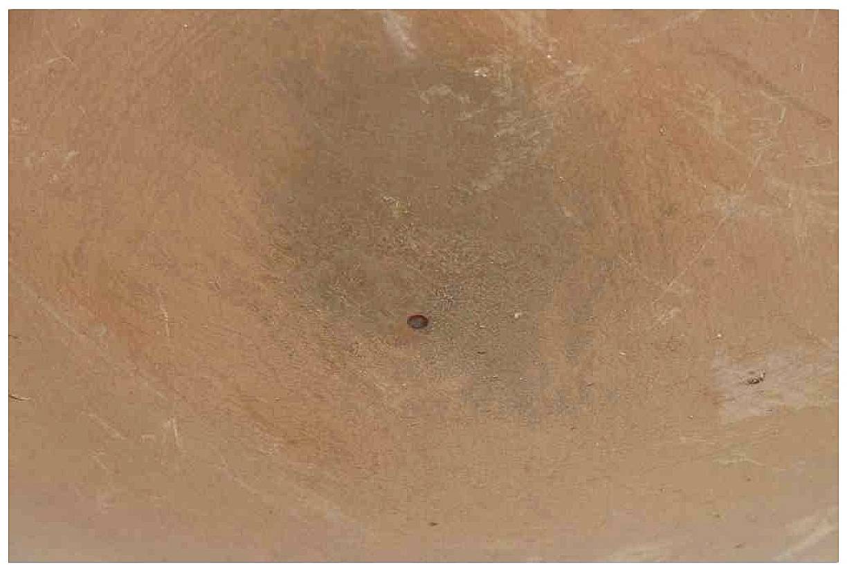 Ein brauner Lehmboden mit einer kleinen dunklen Mulde in der Mitte, möglicherweise eine Vertiefung oder Fußabdruck im weichen Material.