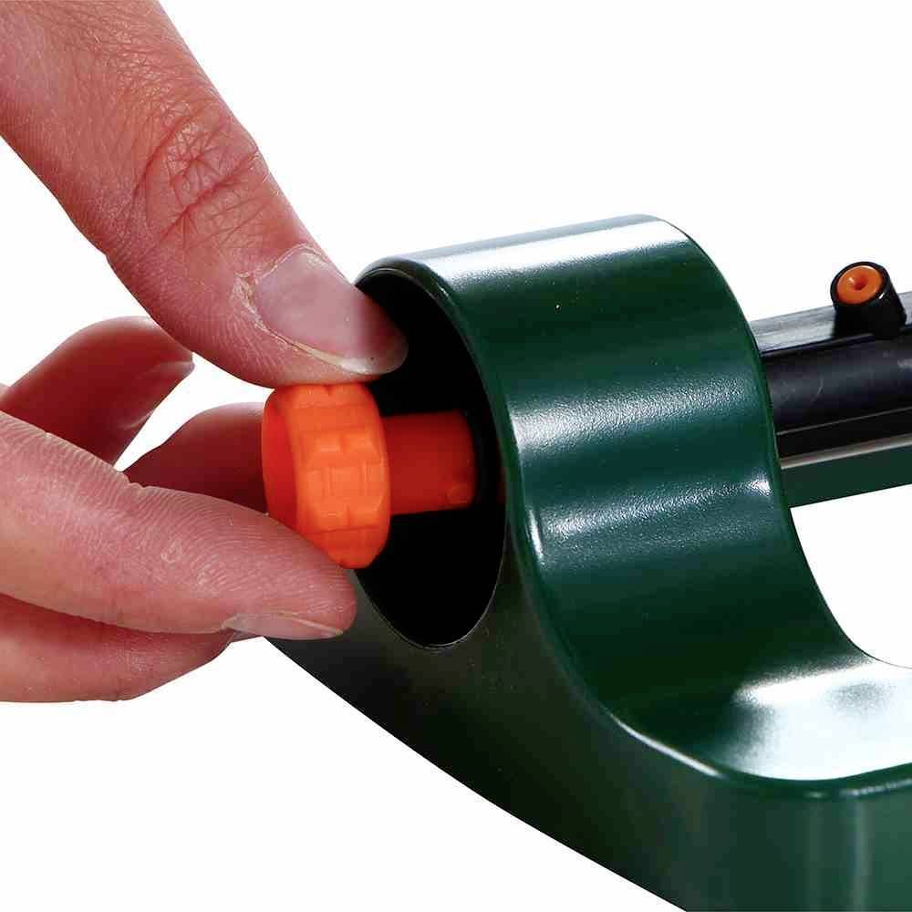 Eine Hand drückt auf einen orangefarbenen Knopf an einem grünen mechanischen Gerät.