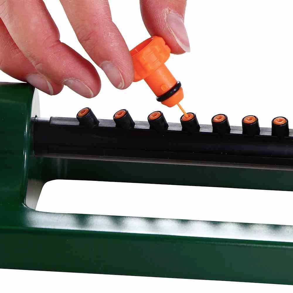 Eine Hand setzt einen orangefarbenen Tropfaufsatz auf ein schwarzes Rohr mit neun Düsen.