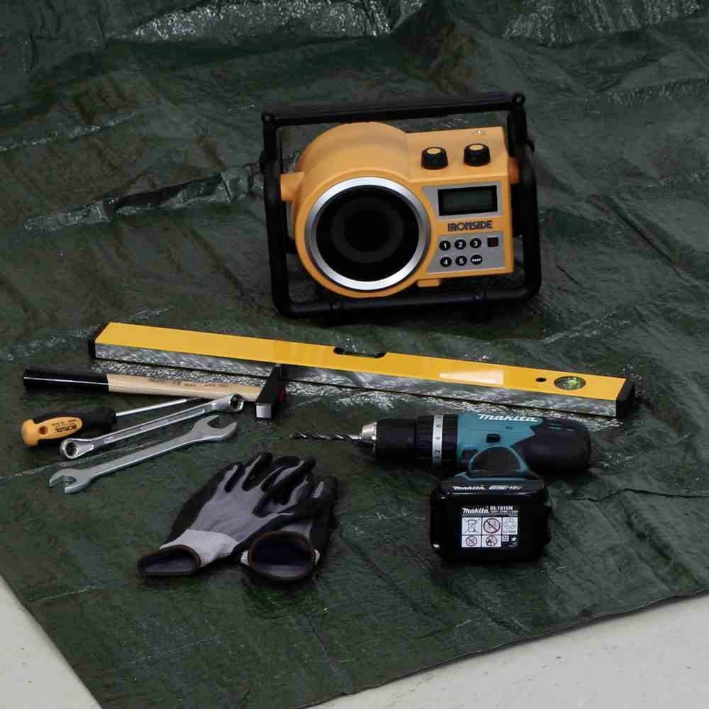 'Einrichten von Werkzeugen auf einer Plane: Laser-Nivelliergerät, Wasserwaage, Schraubenschlüssel, Schutzhandschuhe und Akkuschrauber.'