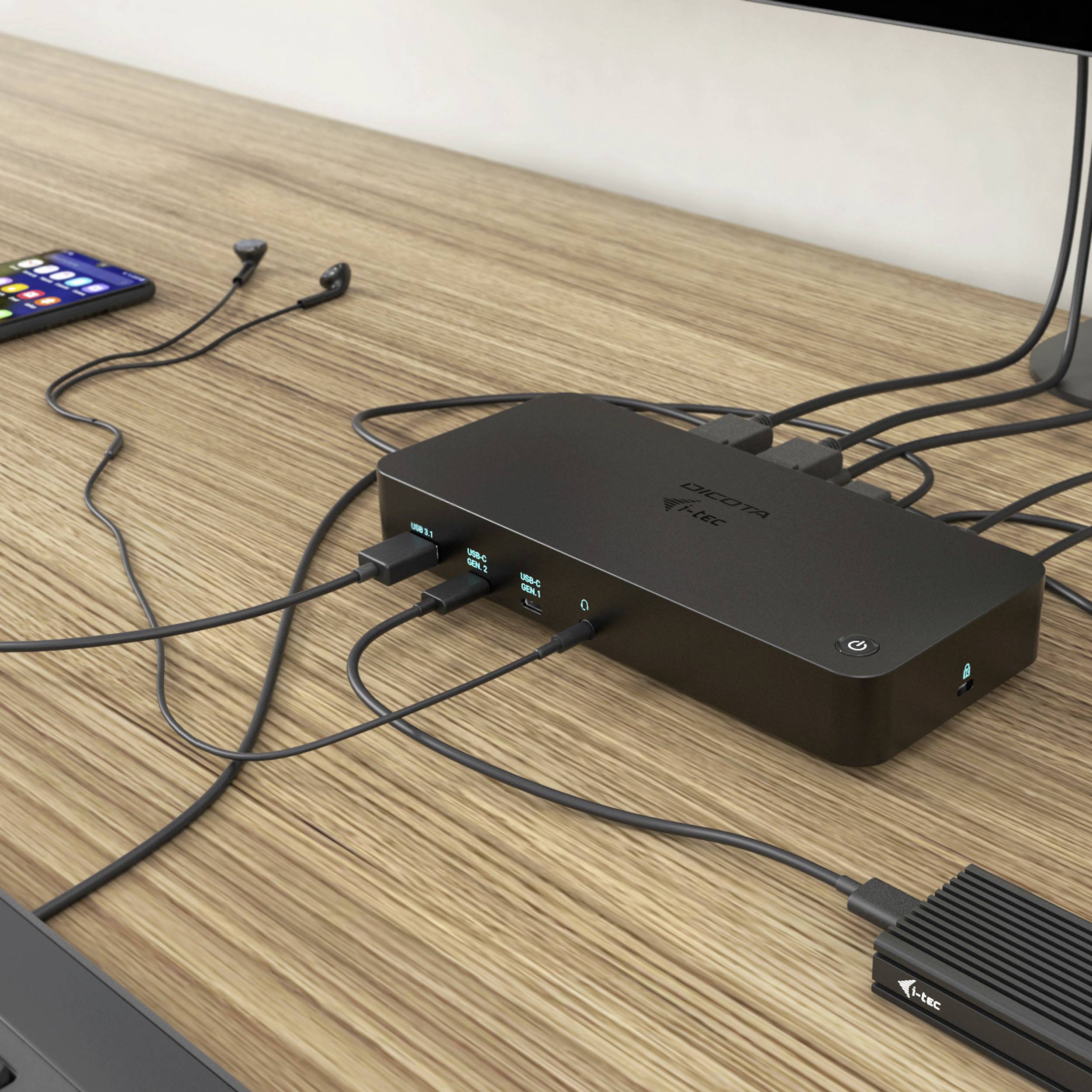 Ein Computer-Dockingstation auf einem Holztisch, angeschlossen an mehrere Kabel: ein Smartphone mit einem Ladekabel und weitere USB-Geräte.