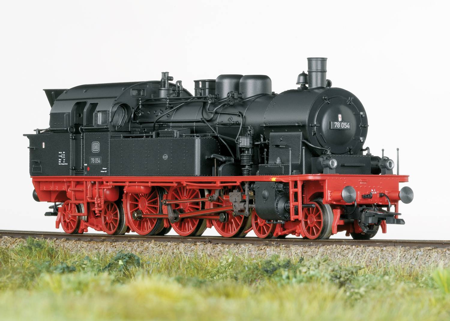 Eine schwarze Dampflokomotive mit roten Rädern steht auf Gleisen. Sie hat einen runden Kessel und zahlreiche technische Details.