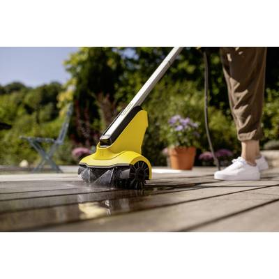 Eine Person reinigt eine Holzterrasse mit einem gelben Hochdruckreiniger an einem sonnigen Tag. Im Hintergrund Pflanzen und ein blauer Stuhl.