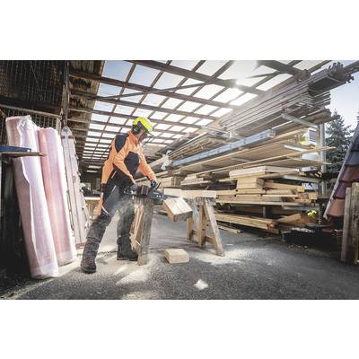 Eine Person sägt in einer Werkstatt Holz mit einer Elektrosäge. Im Hintergrund sind gestapelte Holzplatten und Balken sichtbar.