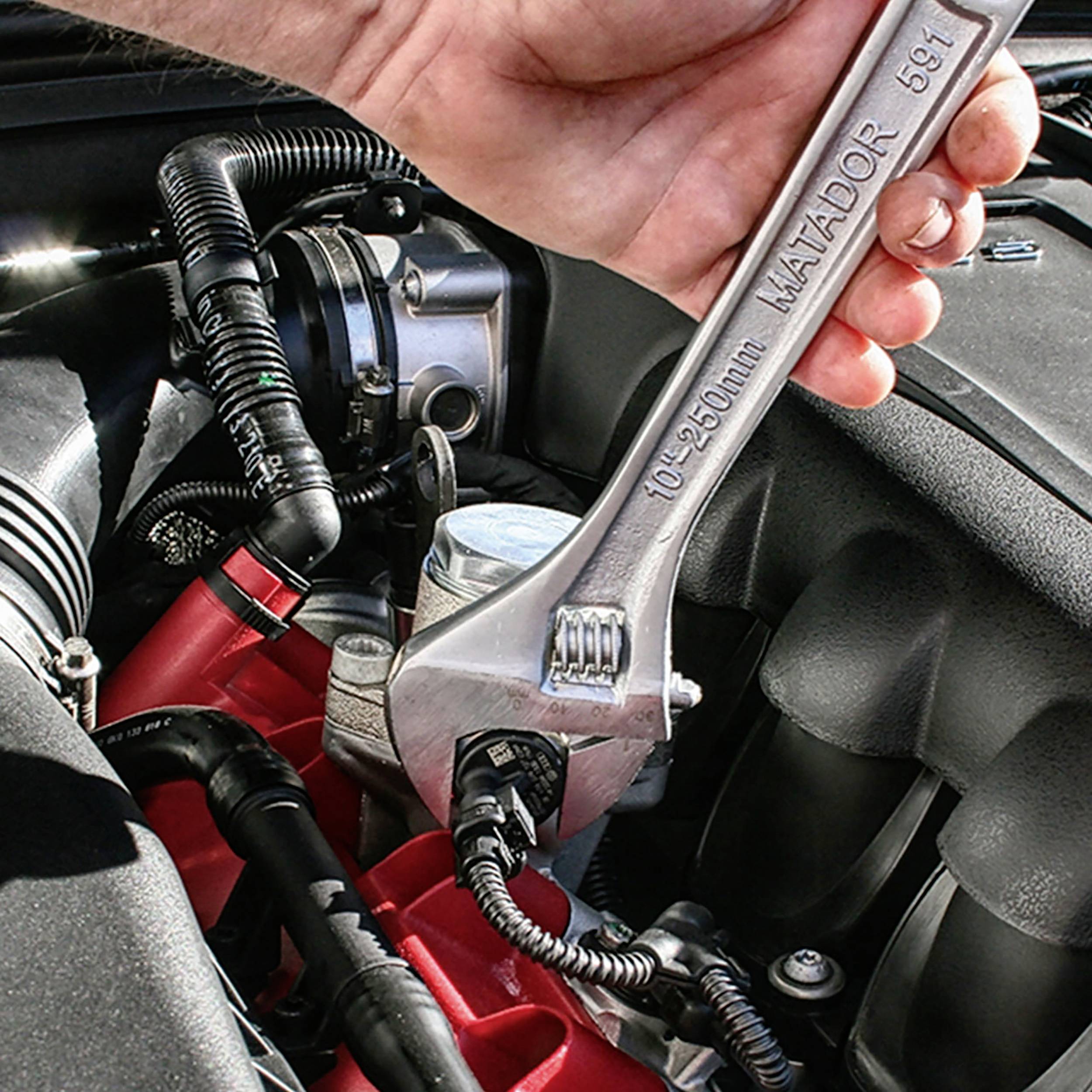 Eine Hand hält einen Schraubenschlüssel, der an einem Kabel an einem Automotor arbeitet, um Wartungsarbeiten durchzuführen.