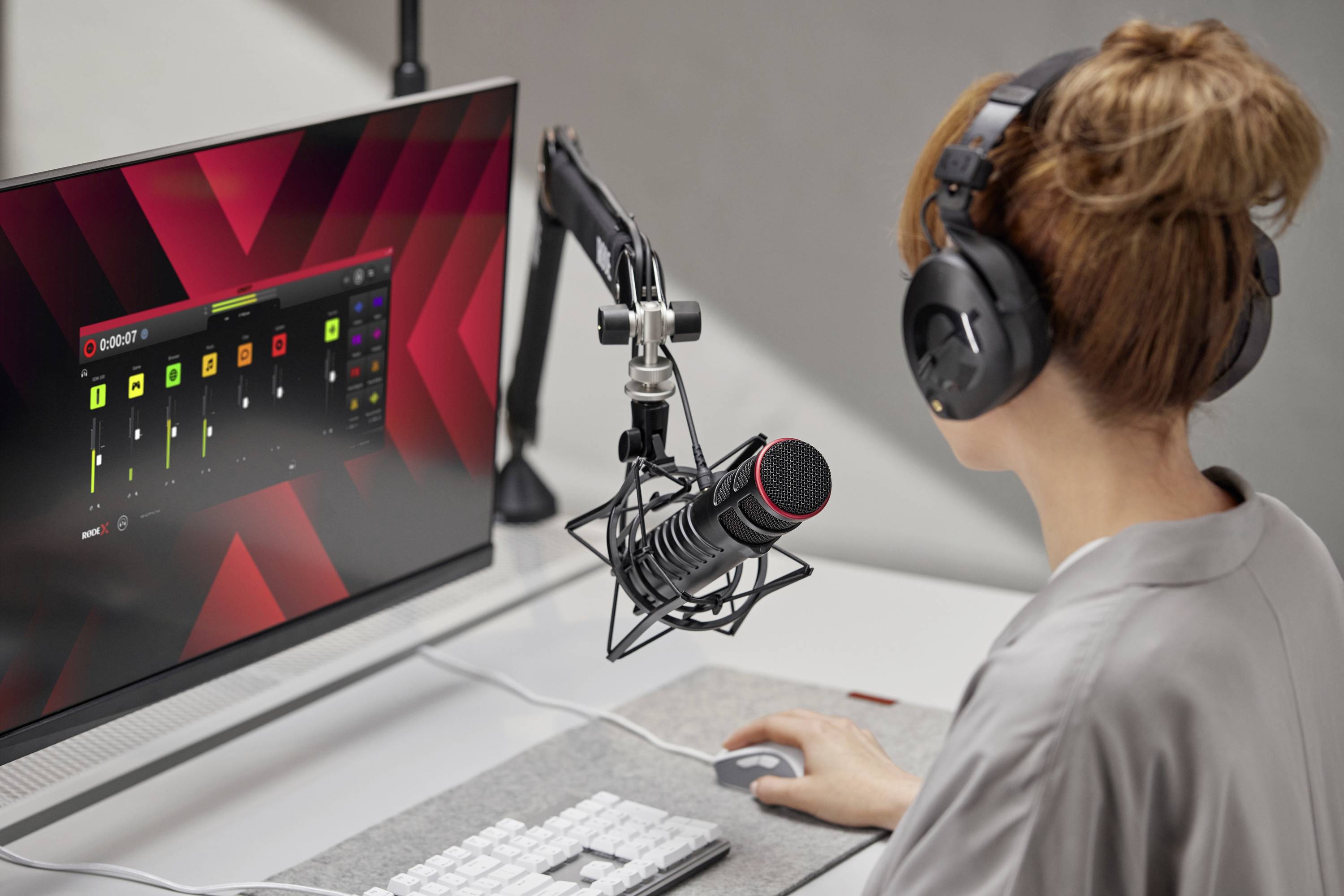 Eine Person mit Kopfhörern sitzt vor einem Computer mit einem Tonaufnahmeprogramm auf dem Bildschirm, spricht in ein Mikrofon.