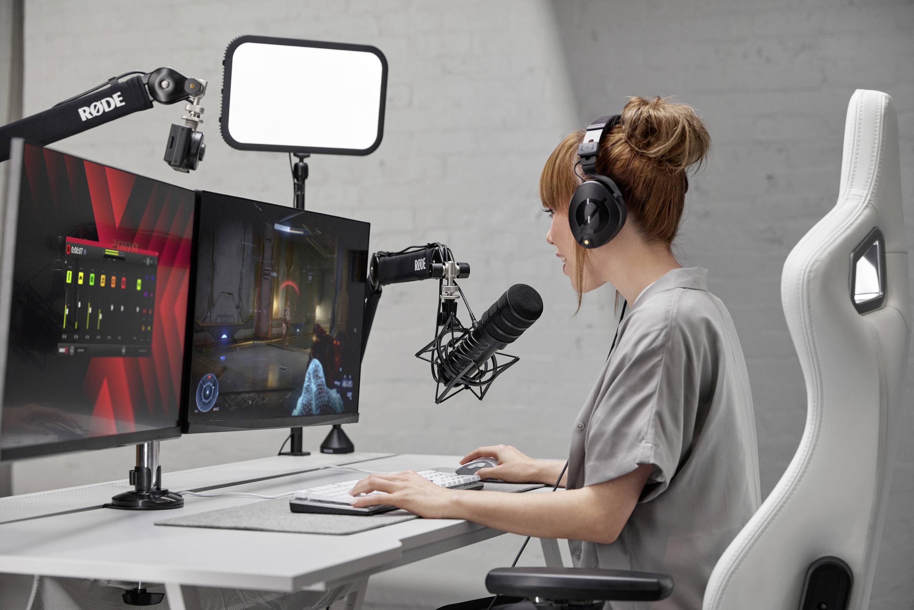 Eine Frau sitzt an einem Schreibtisch mit zwei Monitoren, trägt Kopfhörer und spricht in ein Mikrofon, während sie ein Spiel streamt.