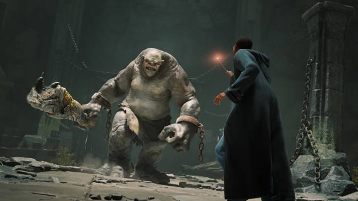 Eine Person in einem Zauberumhang steht einem großen, muskulösen Monster in einer dunklen, steinernen Umgebung gegenüber und hält einen Zauberstab.