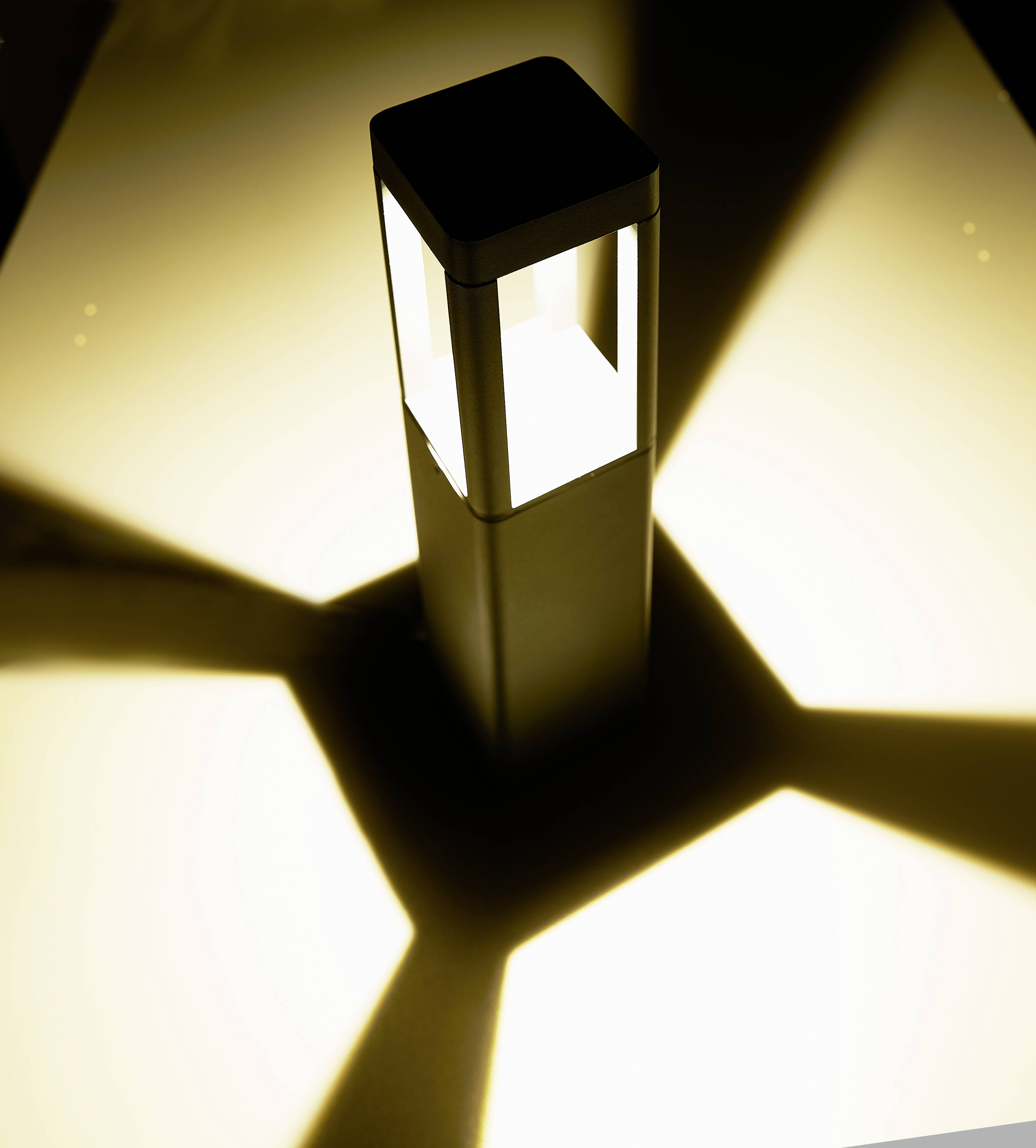 Eine Leuchte wirft sternförmige Schatten auf eine gelbe Oberfläche, die Lampe ist zentral platziert und das Licht ist warm.