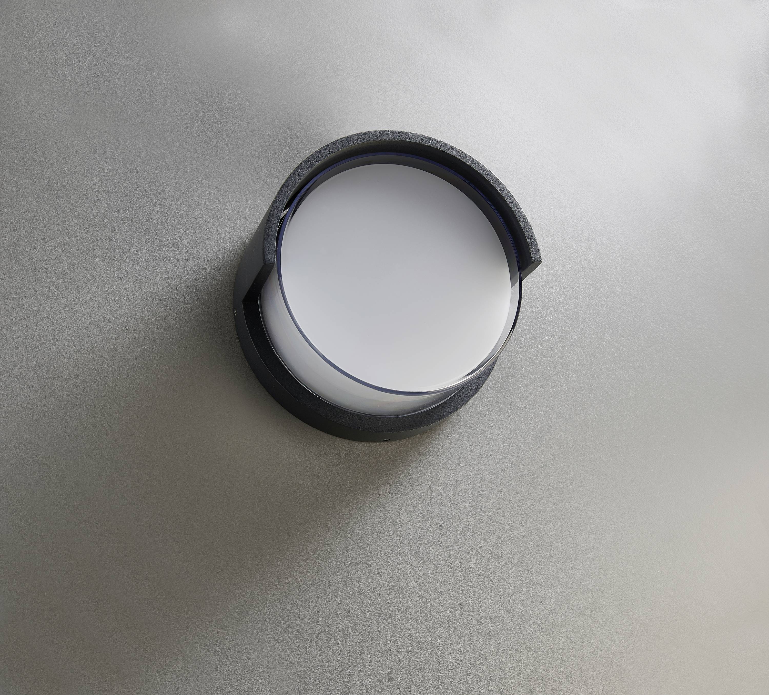 Eine runde, schwarze Wanduhr mit weißem Zifferblatt, ohne sichtbare Zahlen oder Zeiger, hängt an einer grauen Wand.