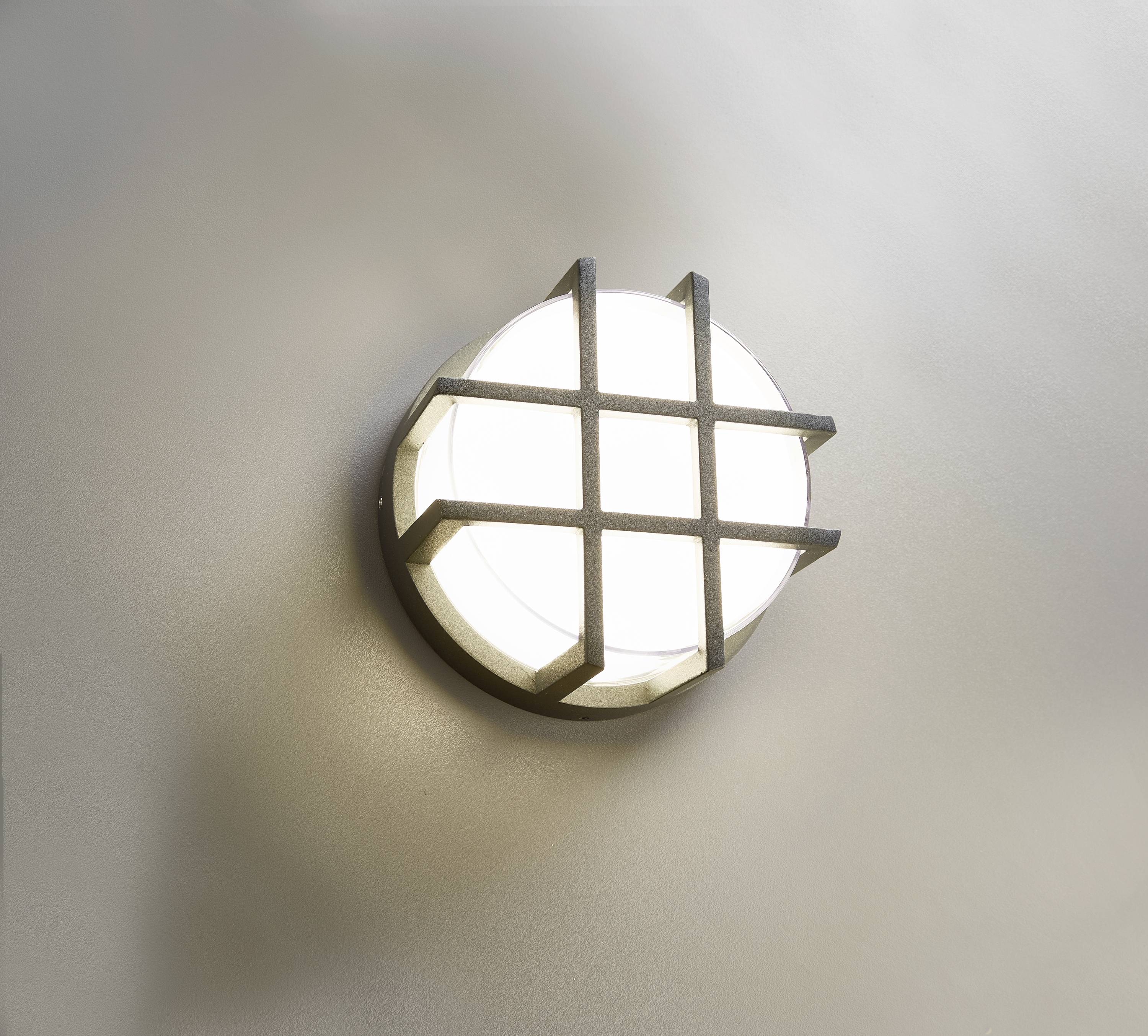 Runde, moderne Wandleuchte mit kreuzförmigem Metallgitter auf hellem Hintergrund angebracht.