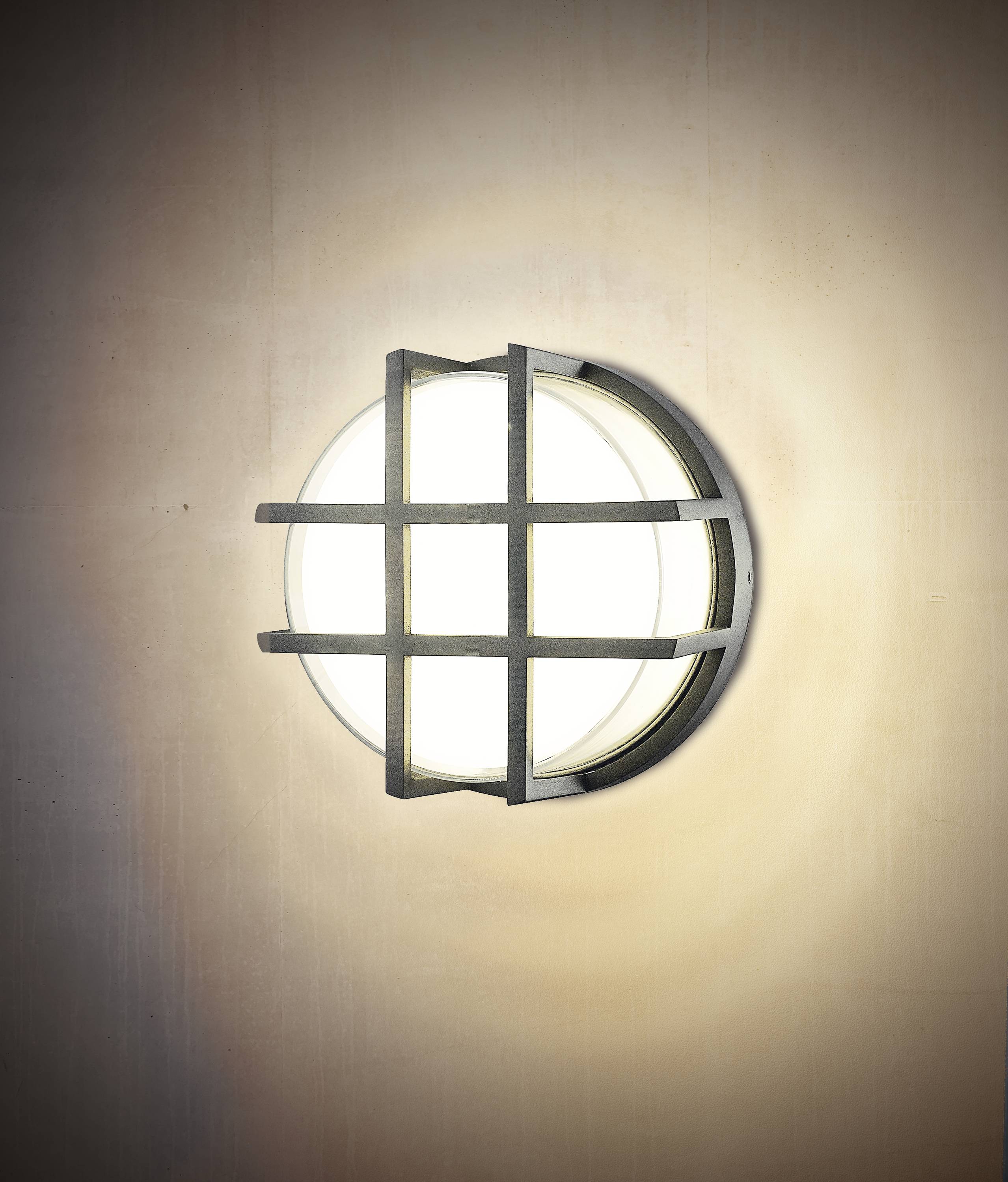 Wandleuchte mit Gitterdesign, rund und modern, leuchtet warmweiß an einer cremefarbenen Wand.