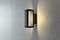 Wandleuchte mit rechteckigem Rahmen, leuchtet warmes Licht auf eine strukturierte Wand. Modernes, minimalistisches Design.