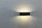 Wandleuchte an einer grauen Wand, die sanftes, diffuses Licht nach oben und unten ausstrahlt, erzeugt eine gemütliche Atmosphäre.