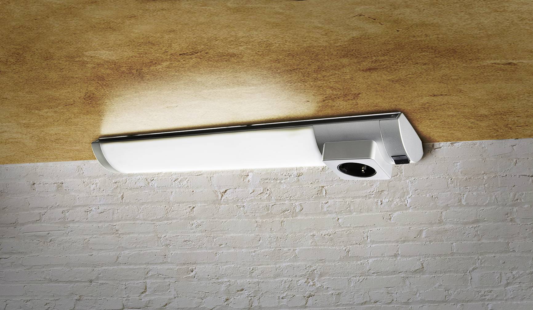 Eine moderne, längliche Deckenleuchte aus Metall und Glas, montiert an einer weißen Backsteinwand unter einer Holzdecke.