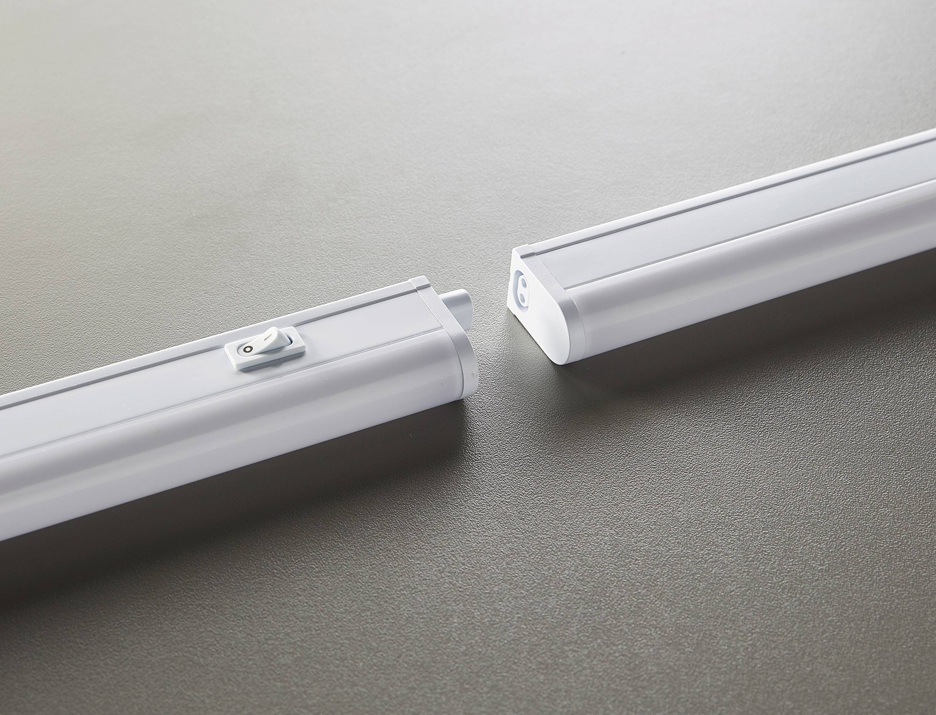 Zwei weiße LED-Lichtleisten liegen auf einer grauen Oberfläche, parallel zueinander, aber nicht verbunden.