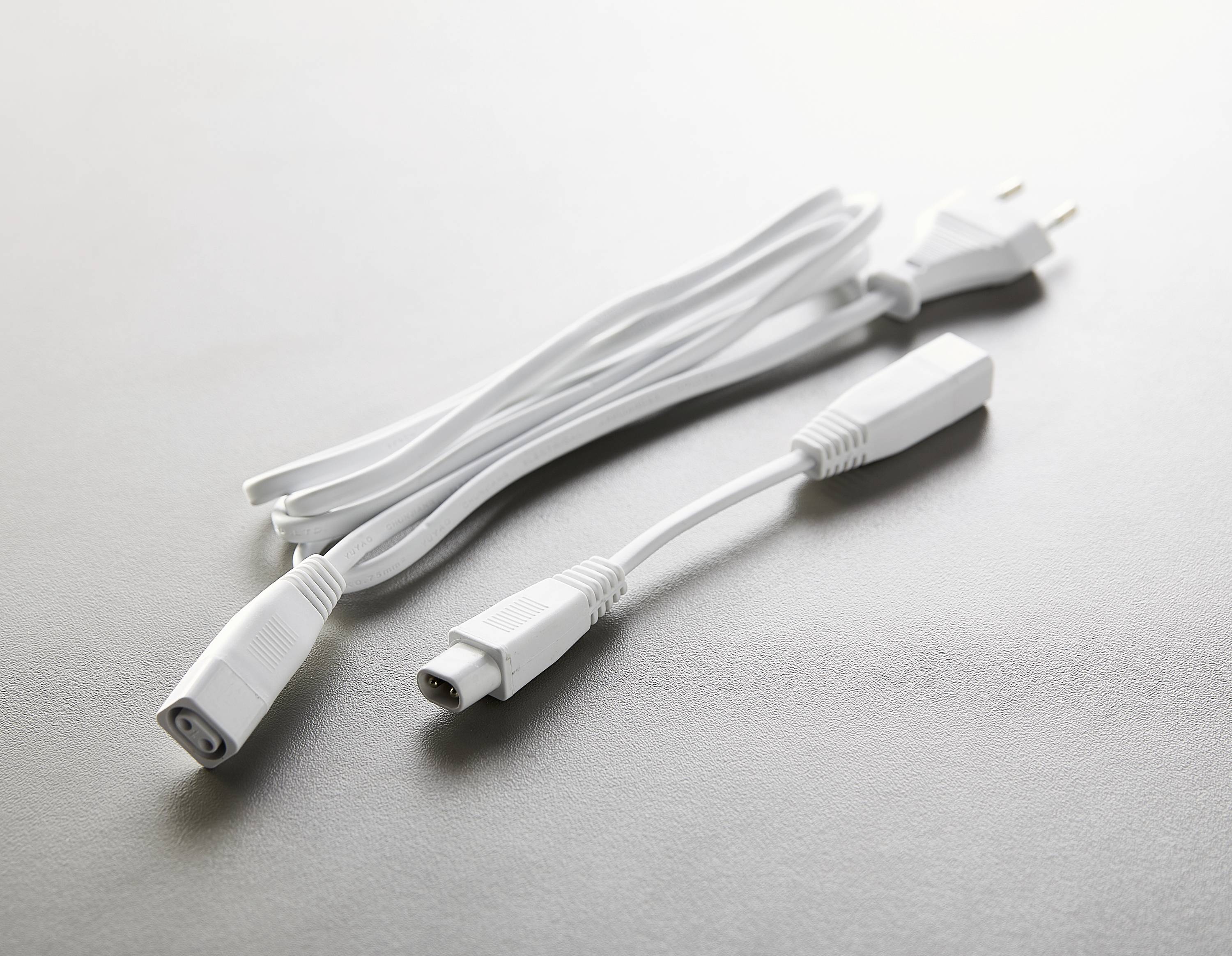 Ein weißes Verlängerungskabel mit zwei Steckern liegt auf einem hellgrauen Hintergrund.