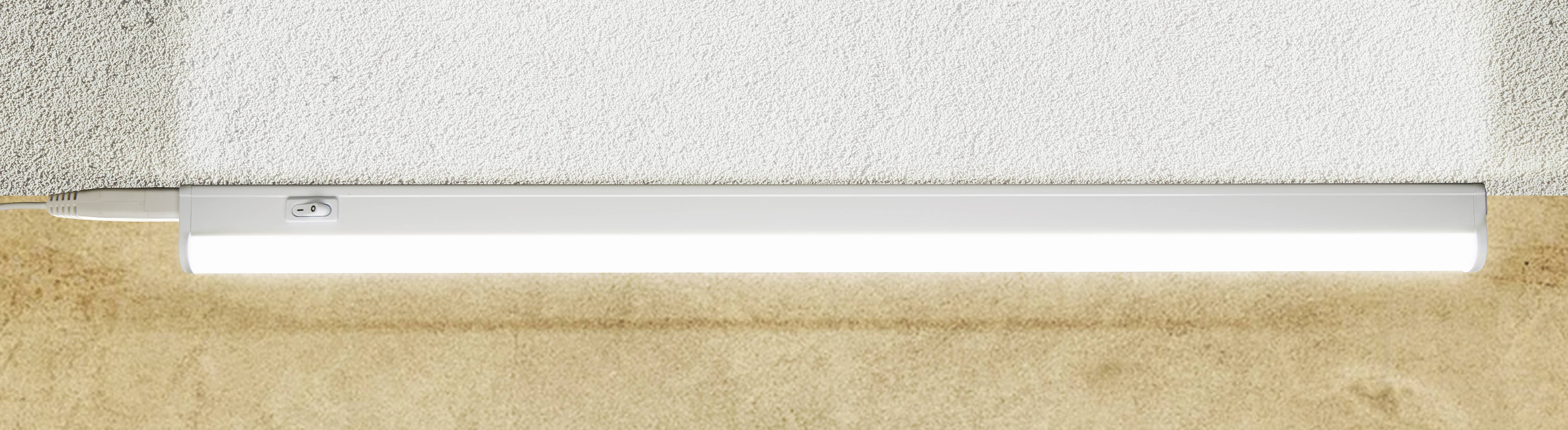 Eine lange, rechteckige LED-Leuchte strahlt an einer Wand aus glattem, hellem Material ab und beleuchtet den Bereich darunter.