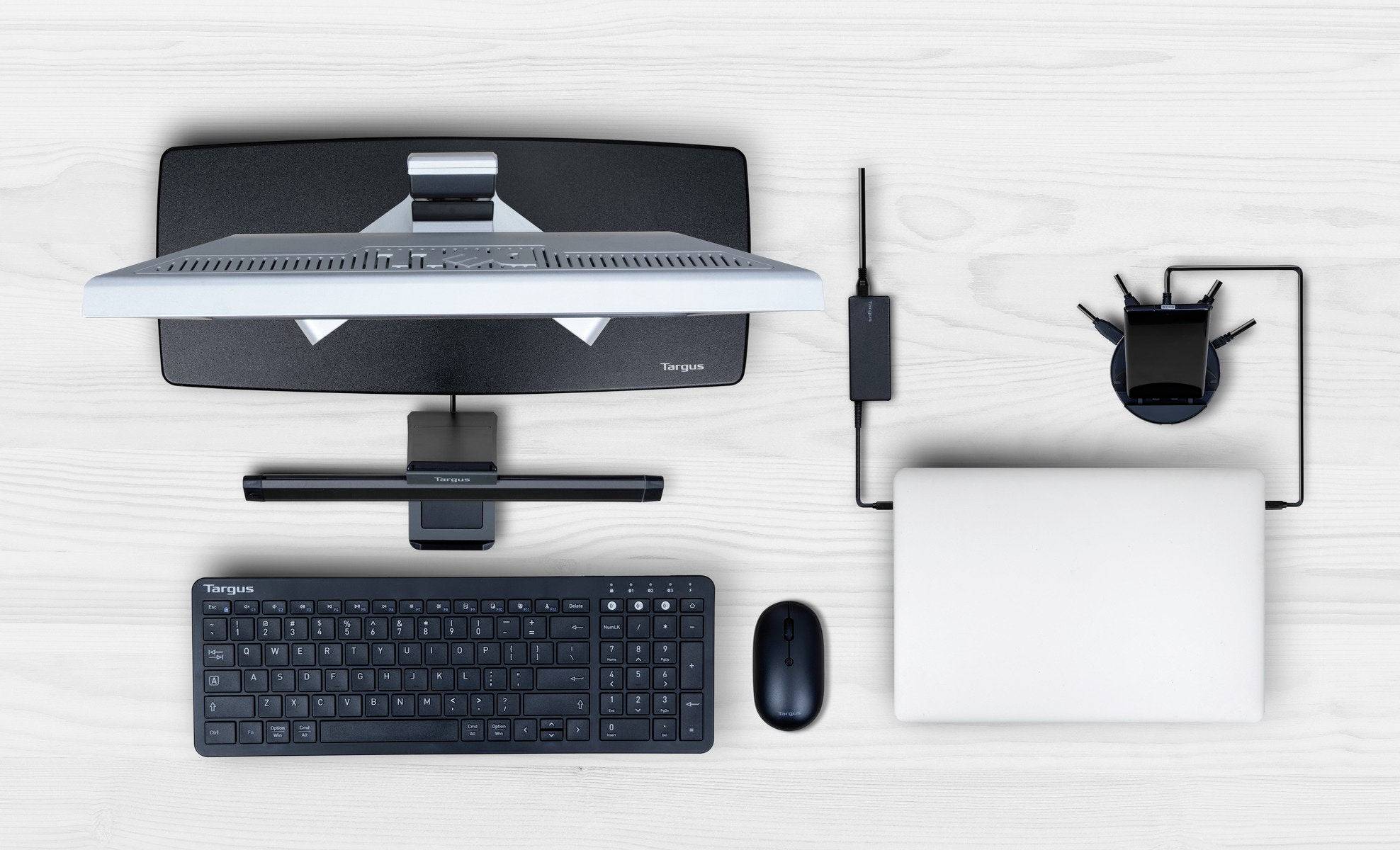 Ein Desktop-Setup von oben: Monitor, Tastatur, Maus, Laptop und Netzwerkadapter auf einem hellen Holztisch.