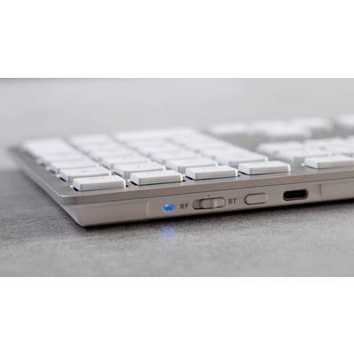 Eine drahtlose Tastatur mit aktivierter Bluetooth-Funktion, erkennbar am blauen Licht. Tasten in Nahaufnahme, grauer Hintergrund.