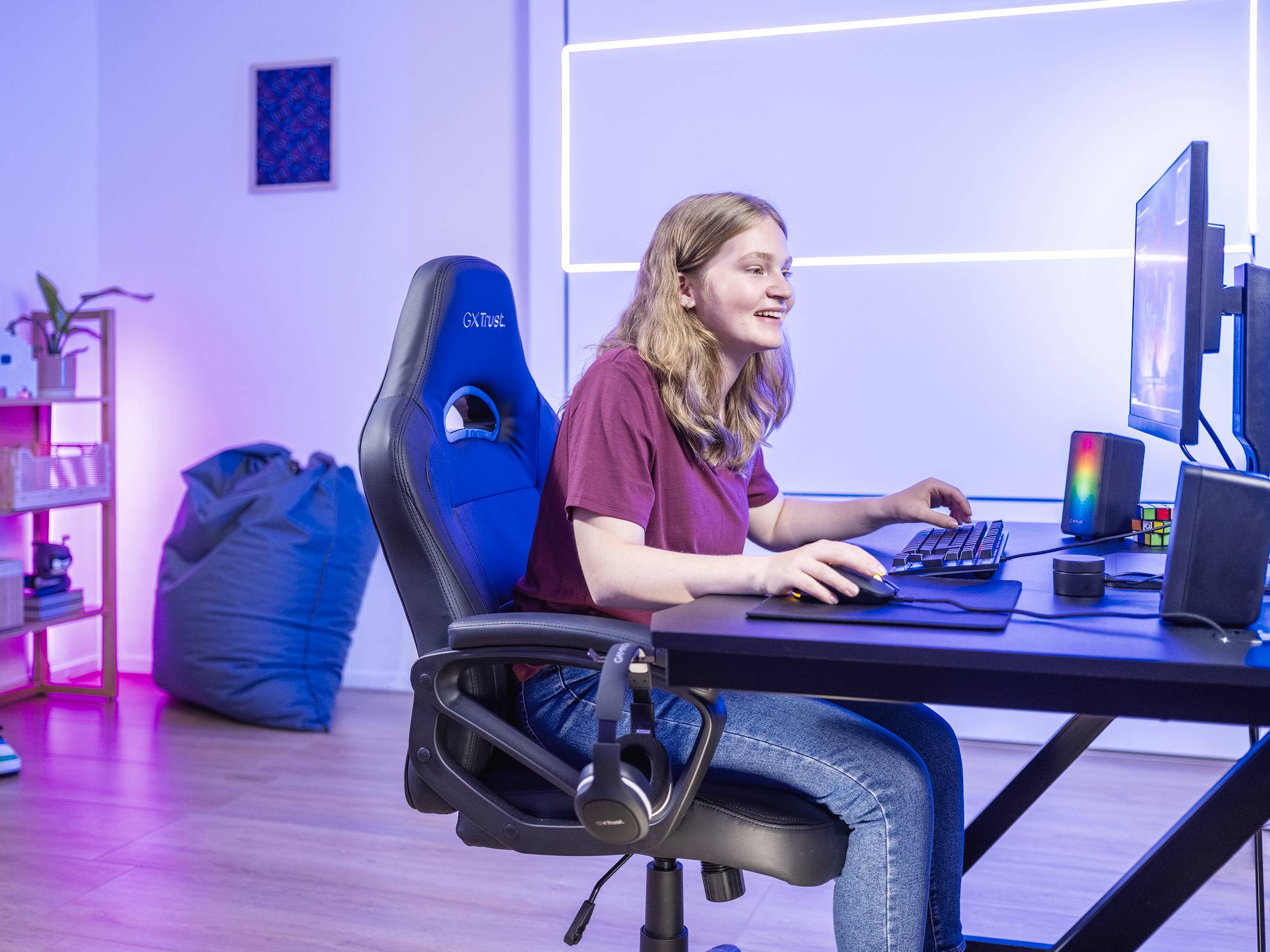 Eine Person sitzt an einem Schreibtisch und spielt an einem Computer, umgeben von buntem Licht und komfortabler Gaming-Ausstattung.