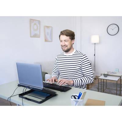 Ein Mann mit gestreiftem Pullover sitzt an einem Tisch und tippt auf einer Tastatur vor einem Laptop, lächelnd in einem Büro.
