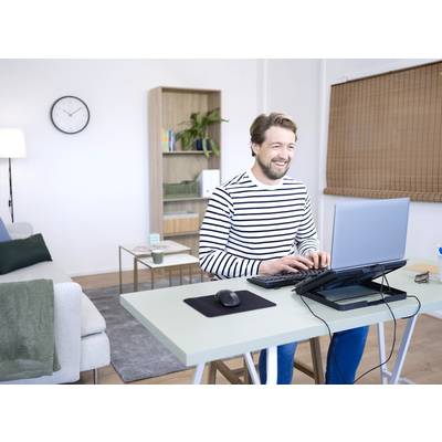 Ein Mann in einem gestreiften Pullover arbeitet lächelnd an einem Laptop in einem modernen Heimarbeitszimmer mit Couch und Regal im Hintergrund.