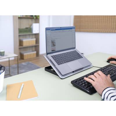 Eine Person tippt auf einer externen Tastatur neben einem Laptop auf einem Schreibtisch, im Hintergrund ein Regal mit Ordnern.