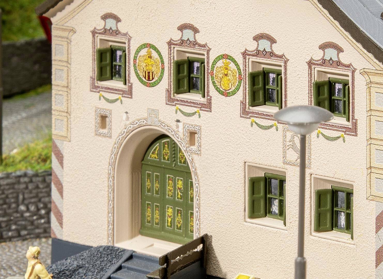 Ein Gebäude mit verzierten Fensterläden und bemalten Fassadenornamenten. Ein Torbogen und eine Laterne im Vordergrund.