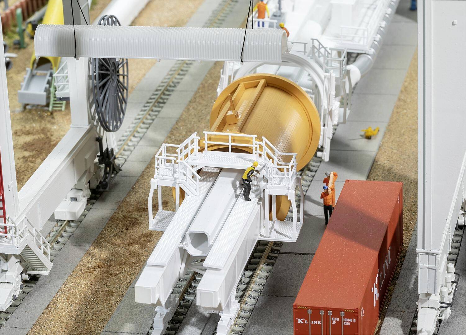 Arbeiter auf einer Baustelle benutzen große Maschinen, um ein Tunnelbohrgerät vorzubereiten. Ein Container steht daneben.