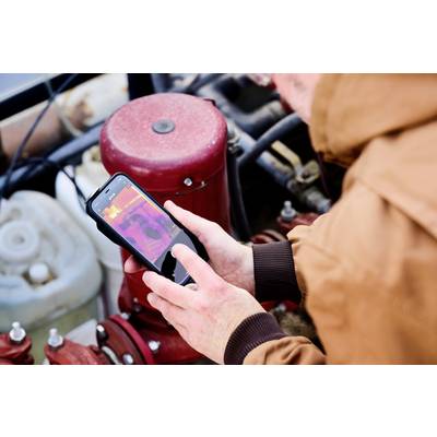Person überprüft Heizsystem mit Smartphone und Wärmebild-App. Rote, pinke und weiße Farben zeigen Temperaturbereiche.