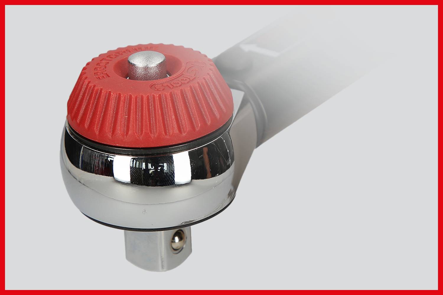 Ein verchromter Ratschenkopf mit rotem Gummigriff, teilweise im Nebel, auf grauem Hintergrund. Geeignet für mechanische Arbeiten.