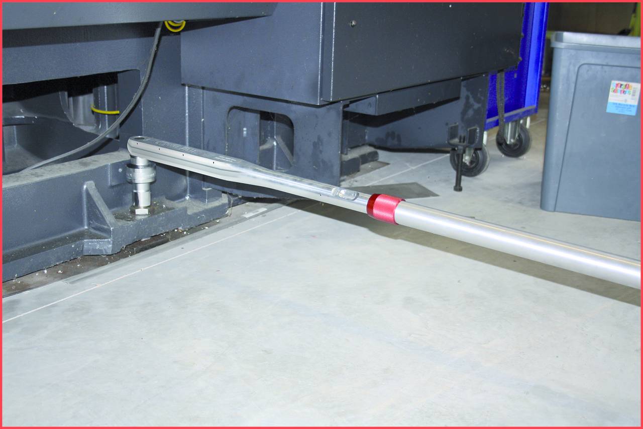Ein metallischer Hebel wird verwendet, um ein großes, graues Maschinengehäuse anzuheben. Der Boden ist aus Beton.