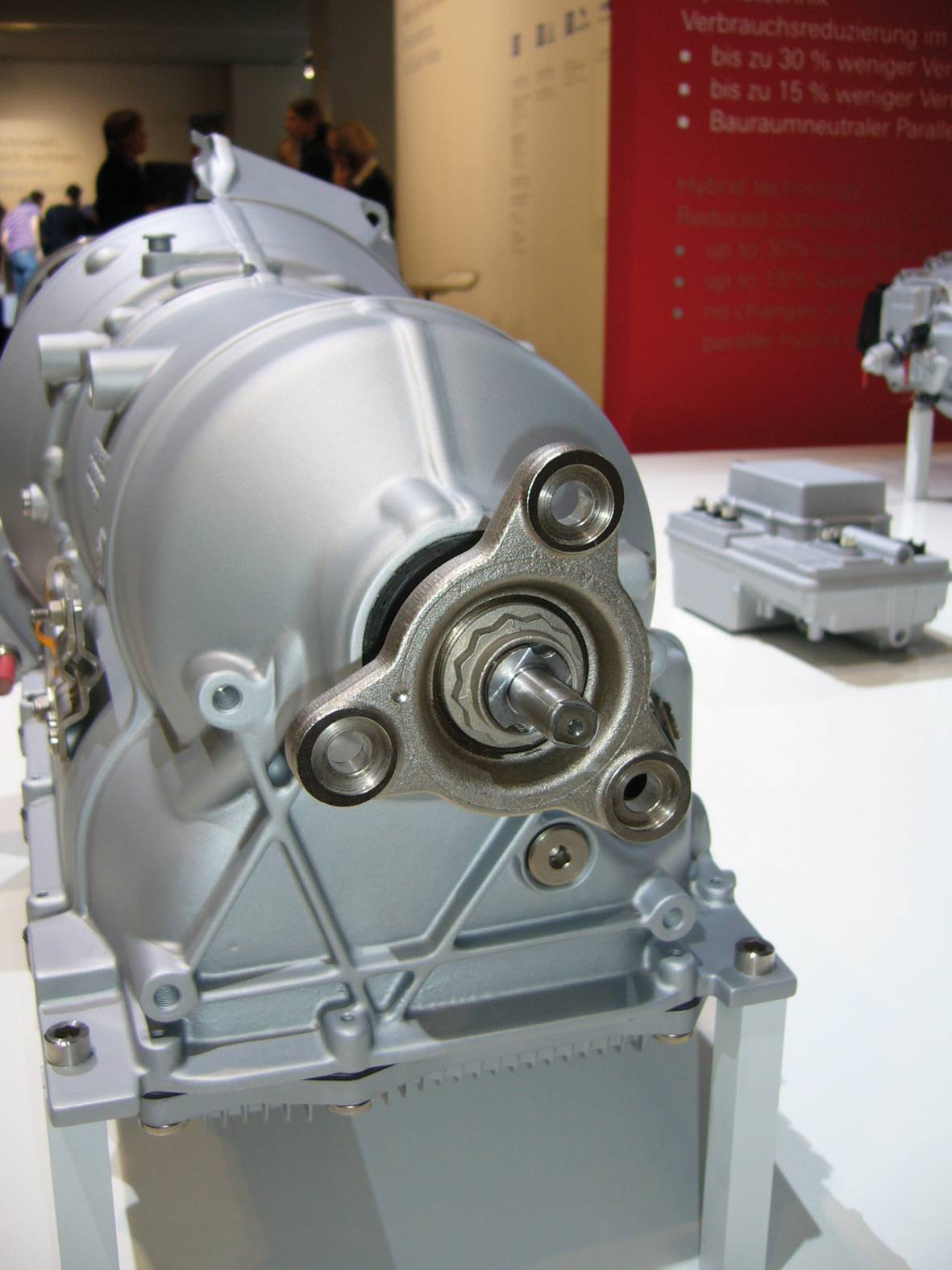 Eine silbergraue Maschinenkomponente auf einem Ausstellungsstand. Details im Hintergrund sind unscharf; Fokus liegt auf der Mechanik.