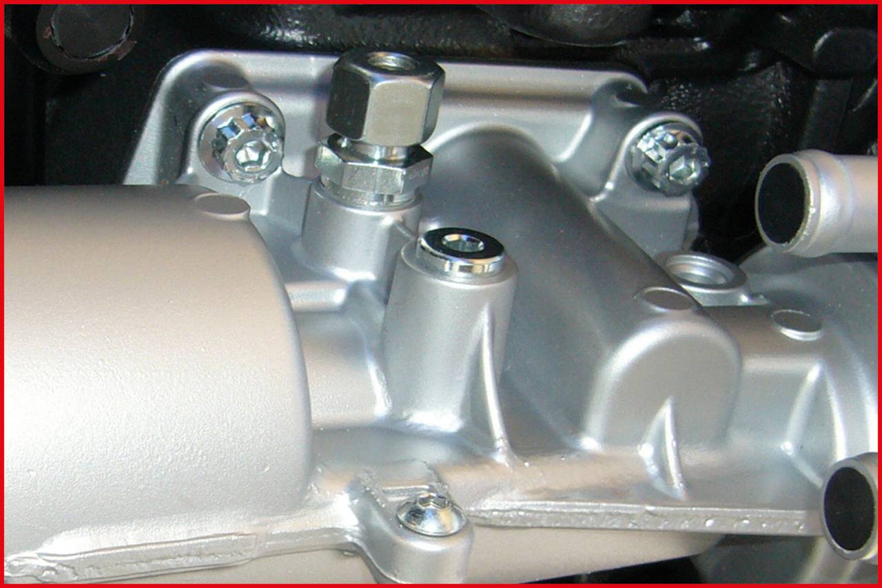 Ein Nahaufnahme eines silbernen Maschinenteils mit Schrauben und Bolzen, möglicherweise Teil eines Motors.