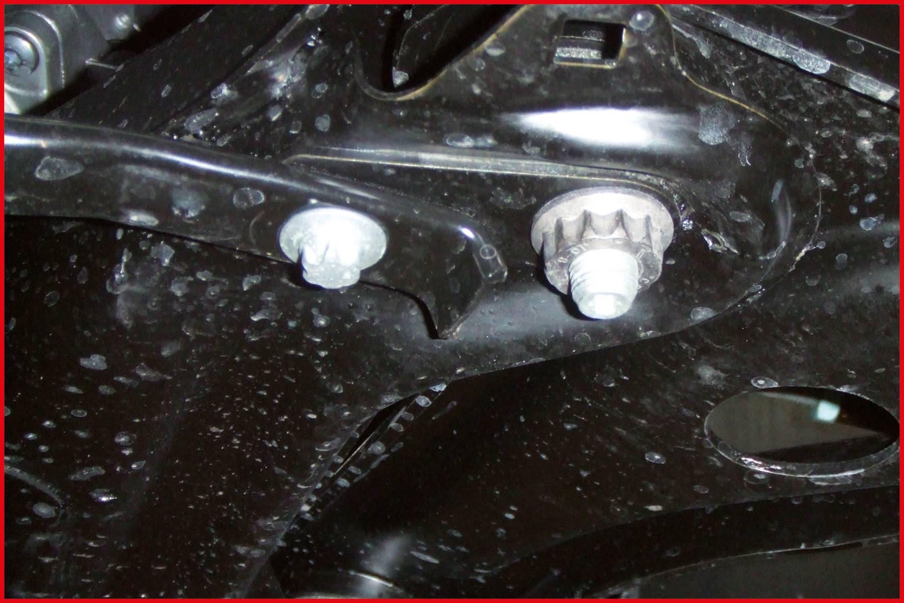 Nahaufnahme von maschinellen Metallteilen mit Muttern und Bolzen. Die Oberfläche ist glatt und schwarz mit Lichtreflexen.