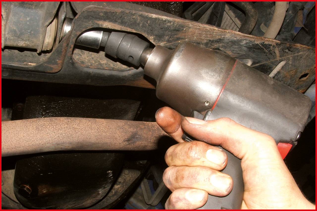 Eine Hand hält eine Schlagbohrmaschine, die an einer Schraube unter einem Auto arbeitet, um das Fahrzeug zu reparieren oder zu warten.