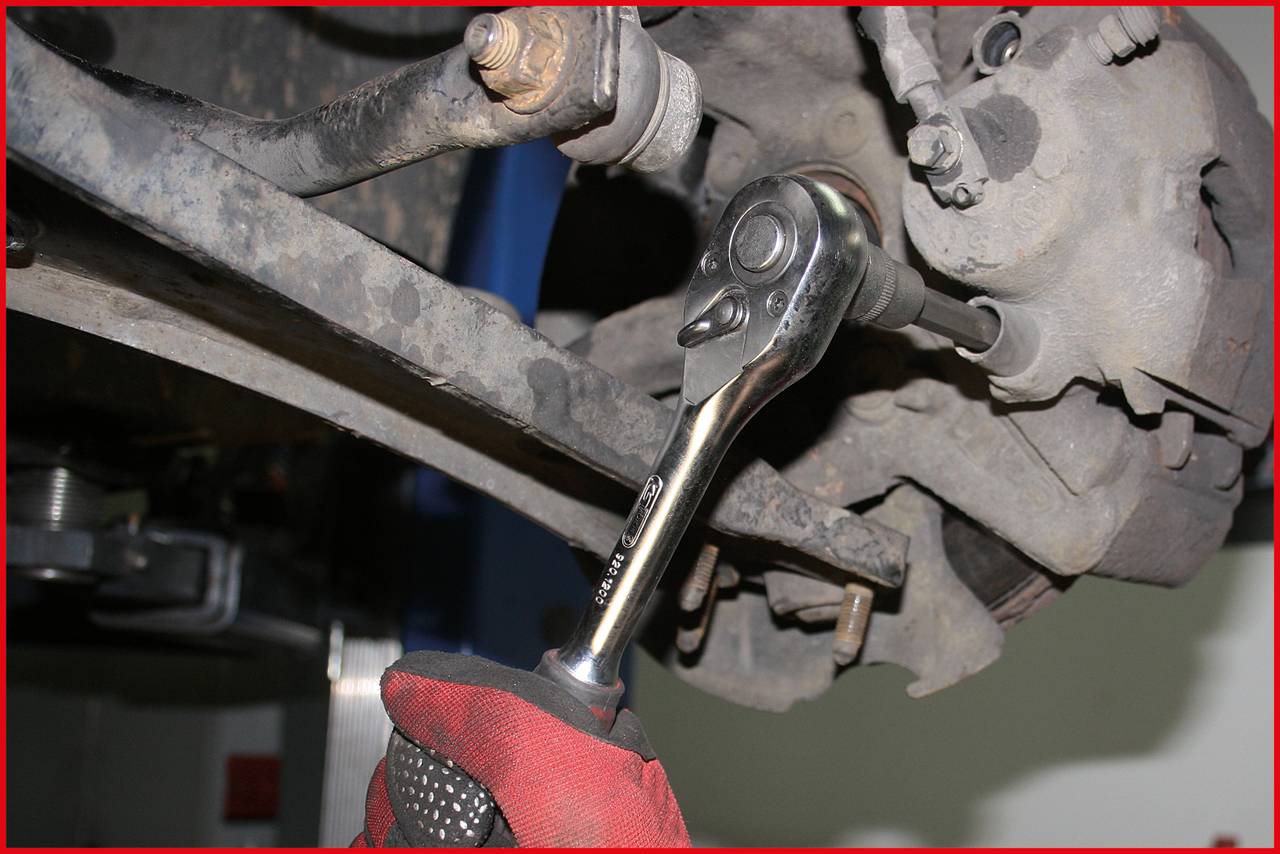 Ein Mechaniker verwendet einen Ratschen-Schlüssel, um an einem Auto zu arbeiten. Der Fokus liegt auf dem Werkzeug und dem Autoteil.