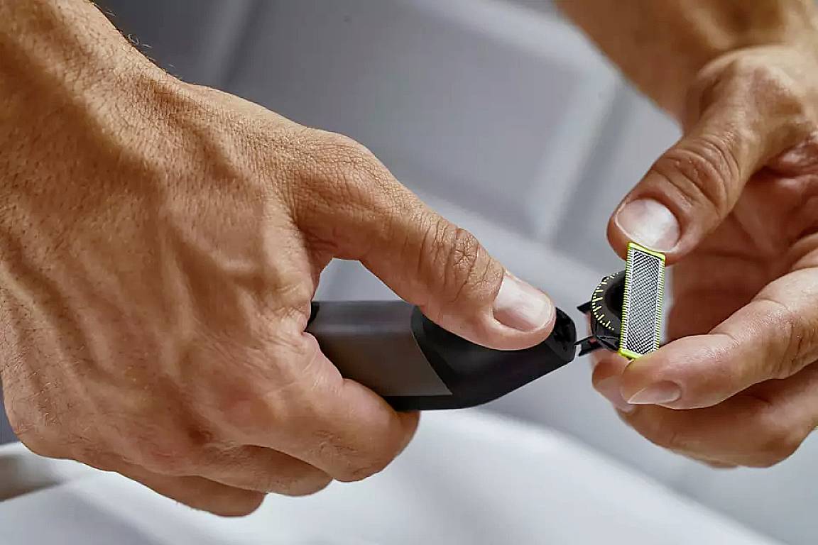 Nahaufnahme von Händen, die einen elektrischen Rasierer mit austauschbarem Kopf halten.