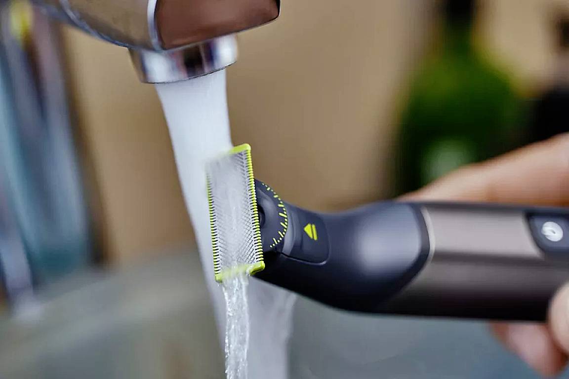 Elektrischer Rasierer mit grünem Klingenschutz wird unter fließendem Wasser gereinigt.