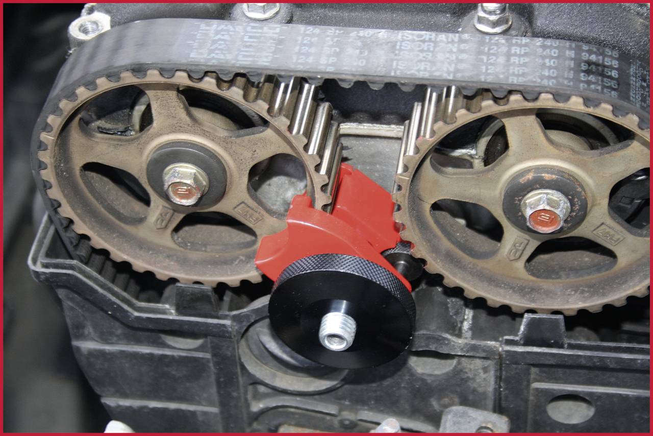 Zwei Zahnräder eines Motors mit einem roten Werkzeug dazwischen, das zur Justierung dient. Das Bild zeigt technische Details des Zahnriemensystems.