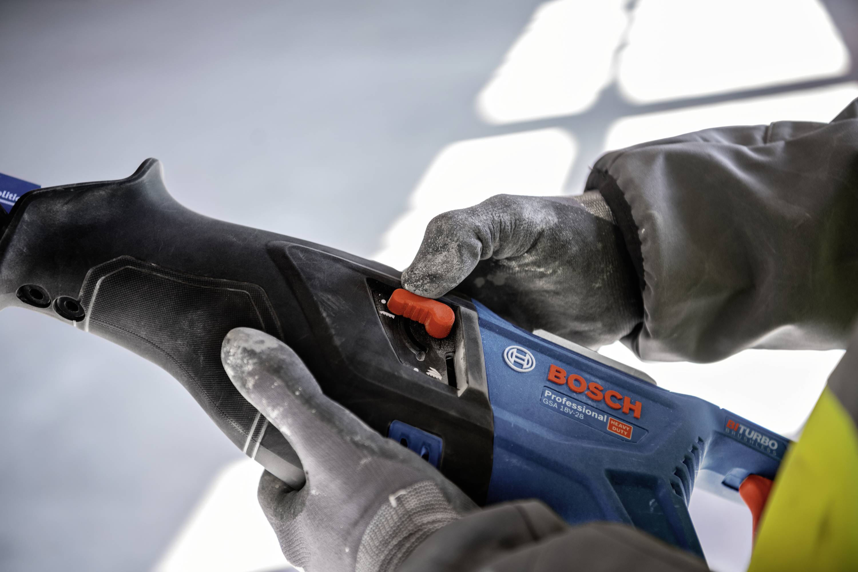 Eine Person hält und bedient ein Elektrowerkzeug mit der Marke 'Bosch' sichtbar. Die Person trägt Arbeitshandschuhe.