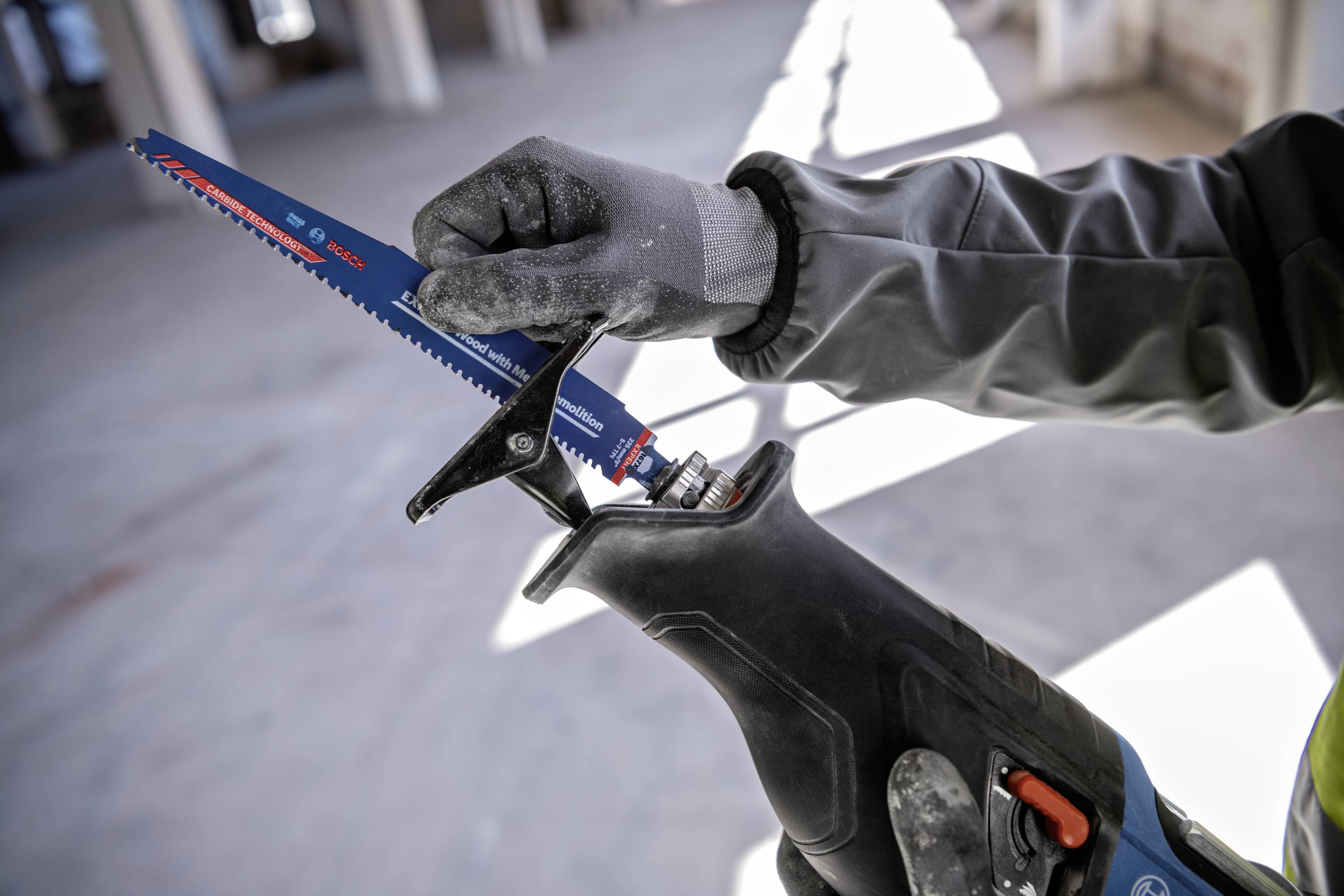 Eine Person mit Handschuhen wechselt das Sägeblatt einer elektrischen Stichsäge in einem hellen, unfertigen Raum.