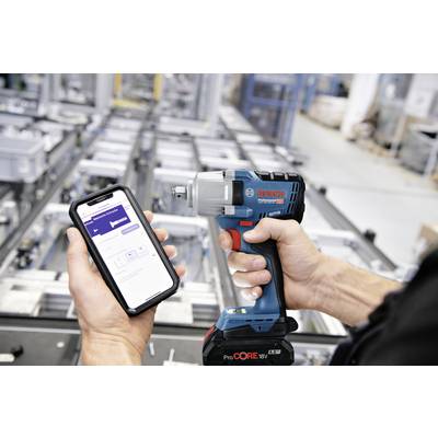 Eine Person hält ein Smartphone mit einer App neben einem Bosch Akku-Schlagschrauber in einer industriellen Umgebung.