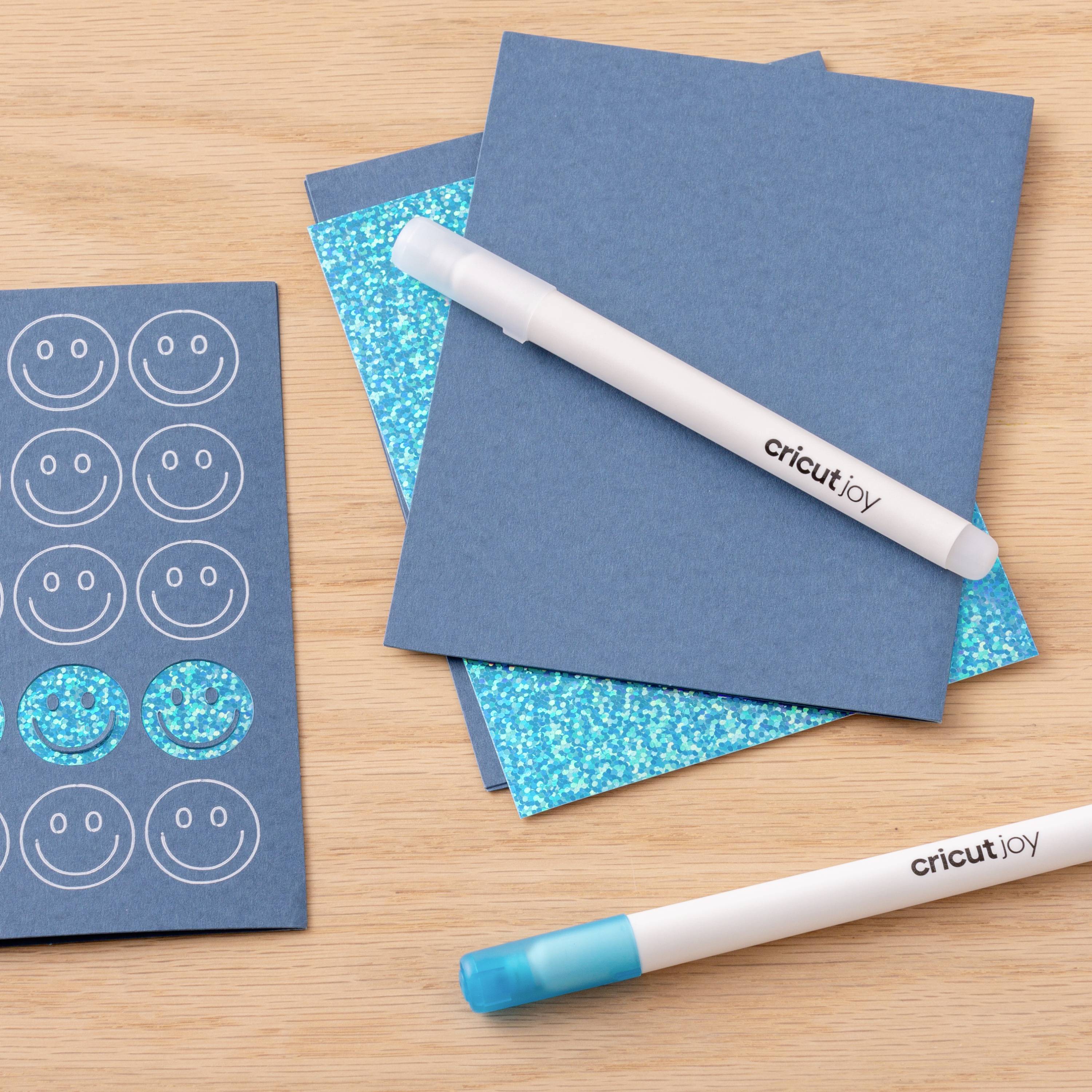 Bastelprojekt mit blauen Papieren, glitzernden Aufklebern und einem weißen Stift auf einem Holztisch; geeignet für Scrapbooking.