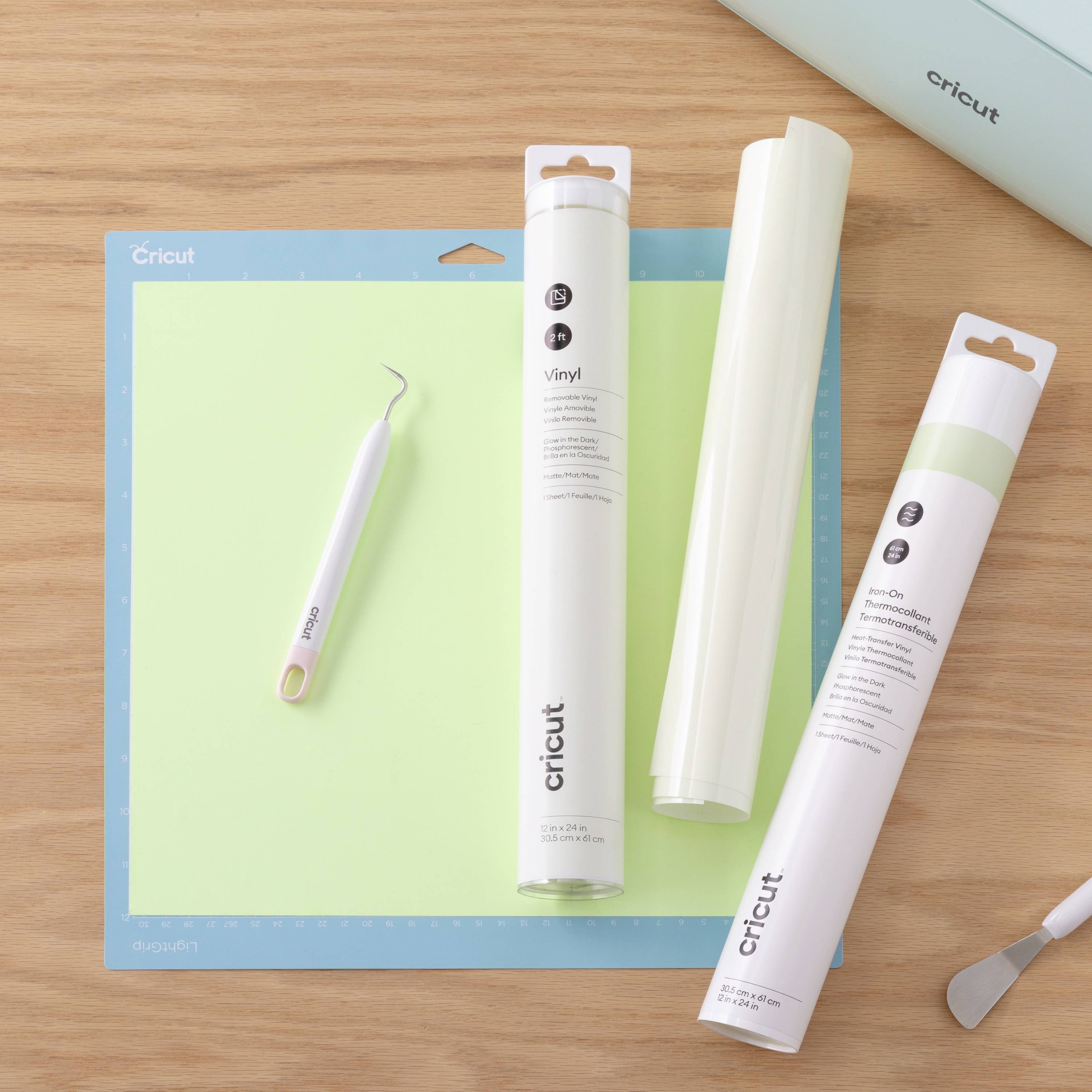 Ein Tisch mit Schneidematte, Vinylfolienrollen und einem Werkzeug. Markenname 'Cricut' auf Werkzeug, Rollen und Matte sichtbar.