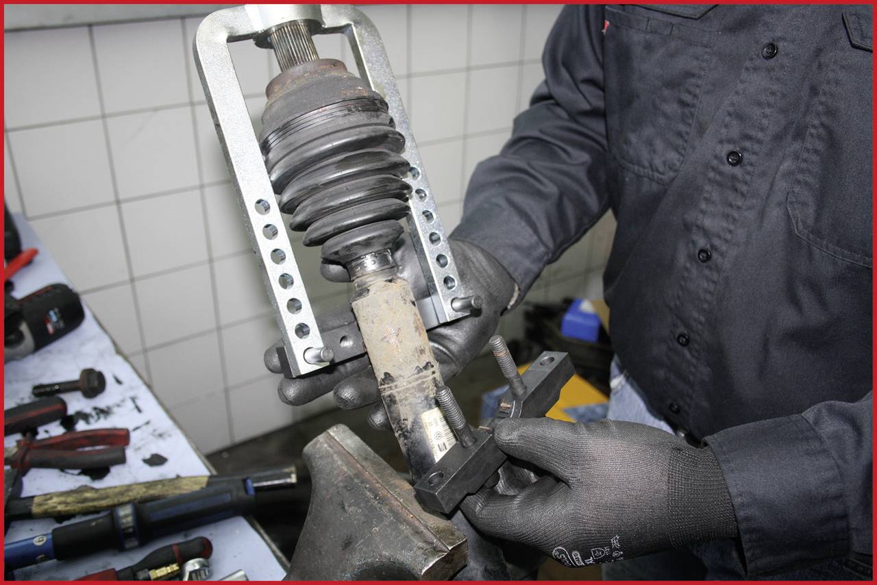 Eine Person repariert ein Fahrzeugdämpfer mit speziellen Werkzeugen. Der Fokus liegt auf dem Dämpfer, der in einer Werkbank eingespannt ist.