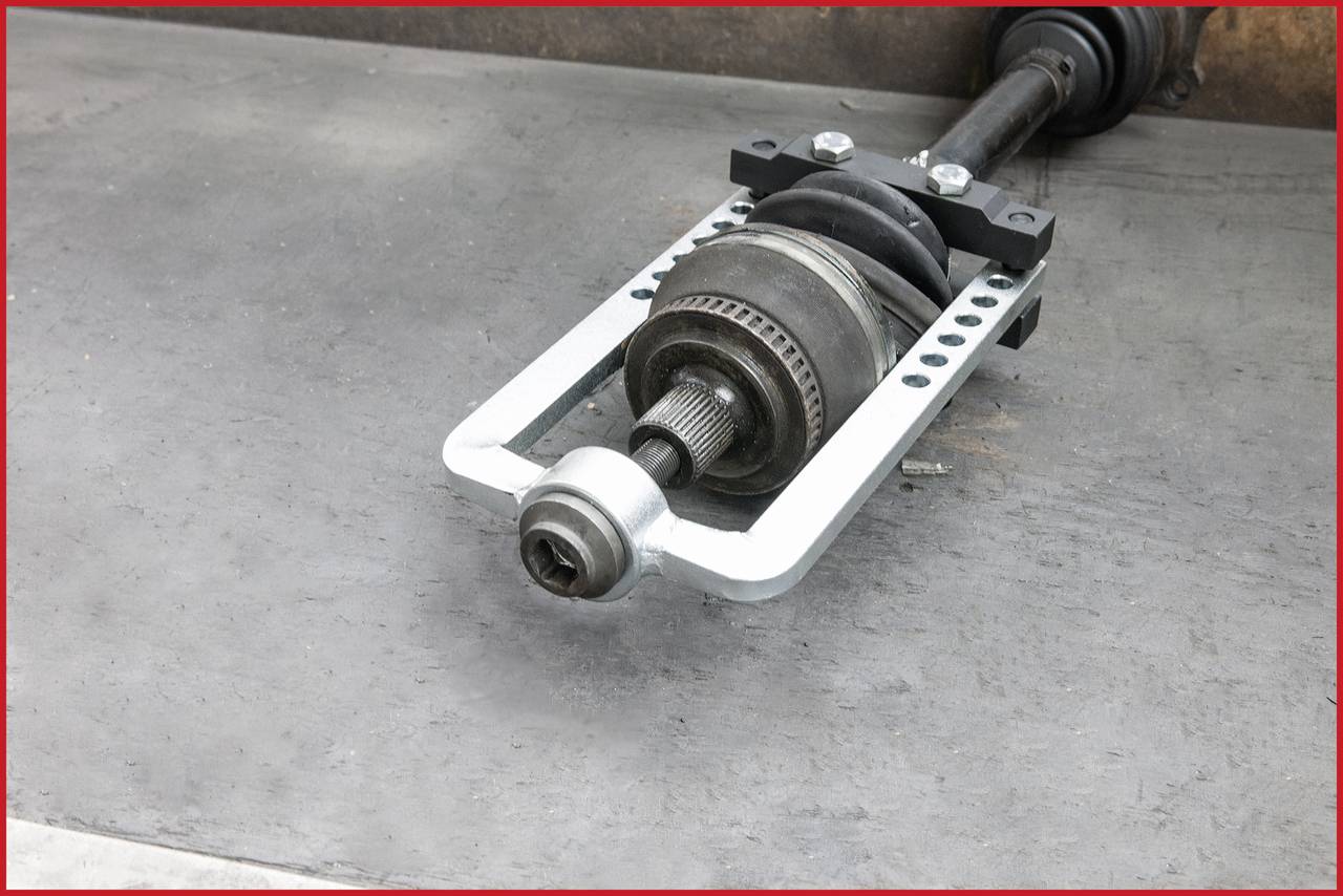 Ein Autoteil, das eine Antriebswelle zeigt, liegt auf einer Werkbank. Sie besteht aus Metall und hat ein Gelenk mit mehreren Schrauben.