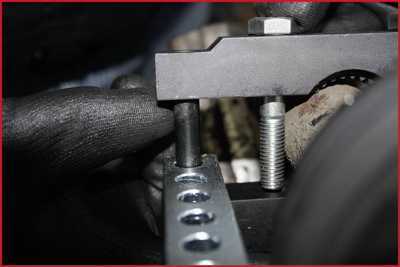 'Nahaufnahme eines Metallrahmens mit Bolzen und Schrauben, gehalten von zwei schwarzen Handschuhen. Fokus auf den Zusammenbau.'